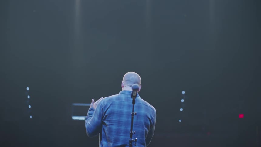 Man stands on lit up stage talking