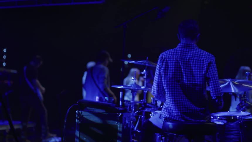 A man plays drums as others perform