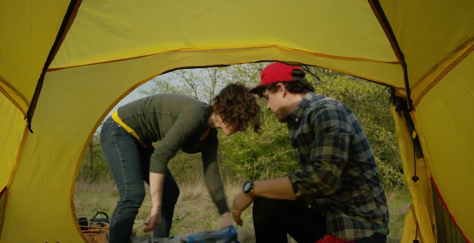 A man and a woman putting their sleeping bags into a small tent