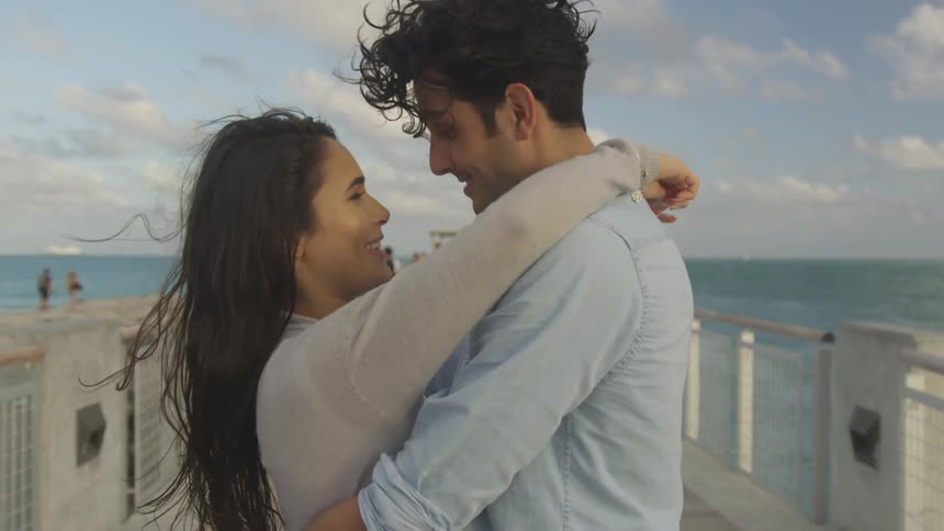 A couple hug while standing on a pier on a sunny day