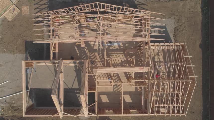A worker dropping a piece of wood at a construction site with the framework of a home being built