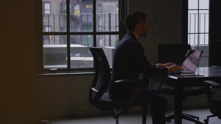 A man works on his laptop by the window in the office