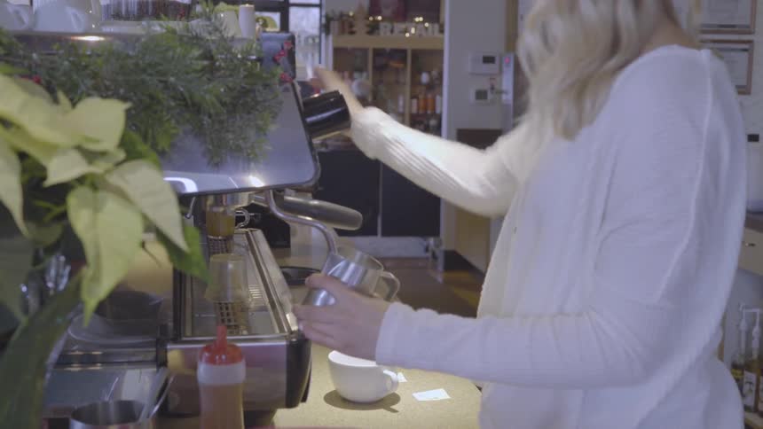 A barista in a coffee shop is making steamed milk for a coffee