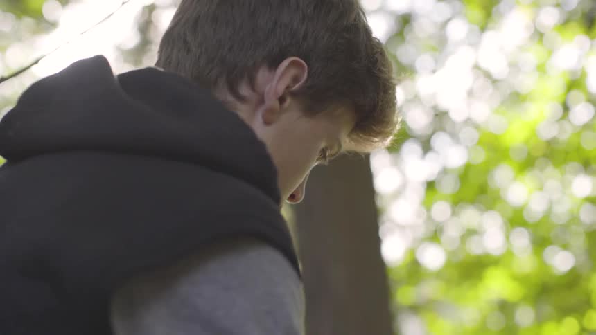Child sits outside by trees looking down