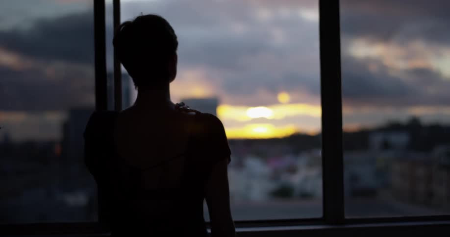 A woman watches the sunset over the city from a window