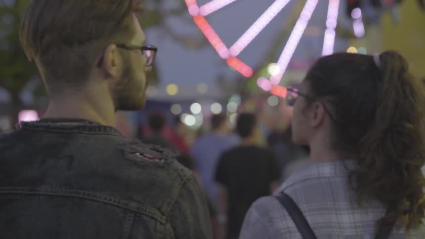 A couple are taking in the sights at a fair at dusk