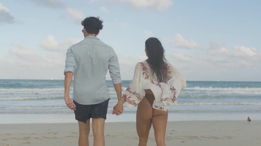 A couple holds hands as they walk toward the ocean