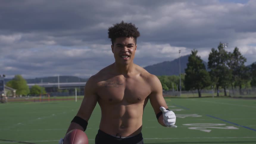 A boy holding a football flexes his muscles