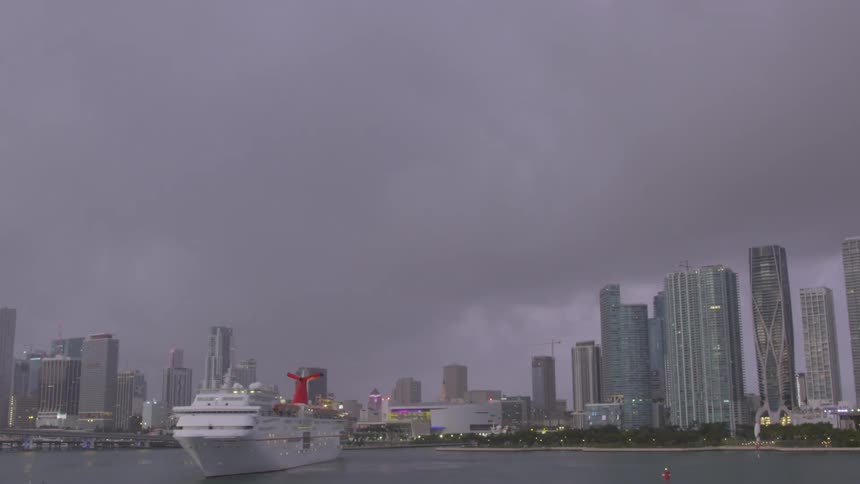 A cruise ship is turning around in a city harbor at dusk