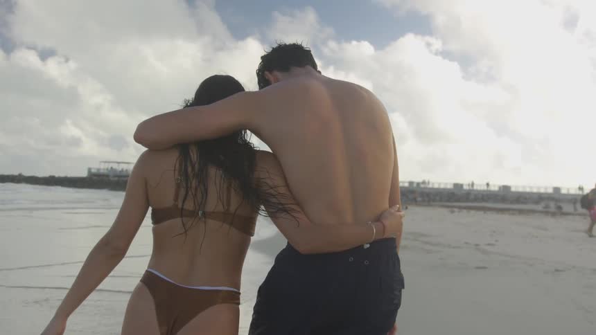 A couple in bathing suits walk into the water with their arms around each other