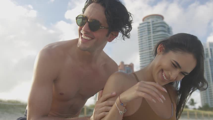 A man and woman laugh together on the beach