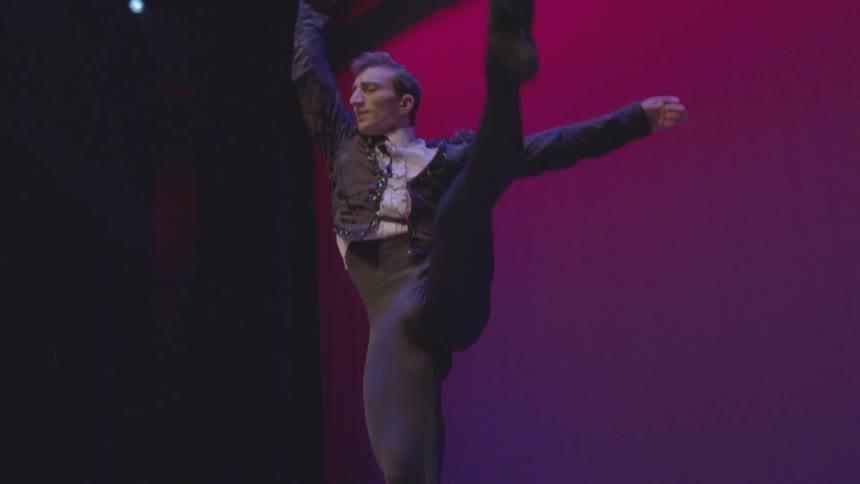 A male ballet dancer leaps and performs on stage