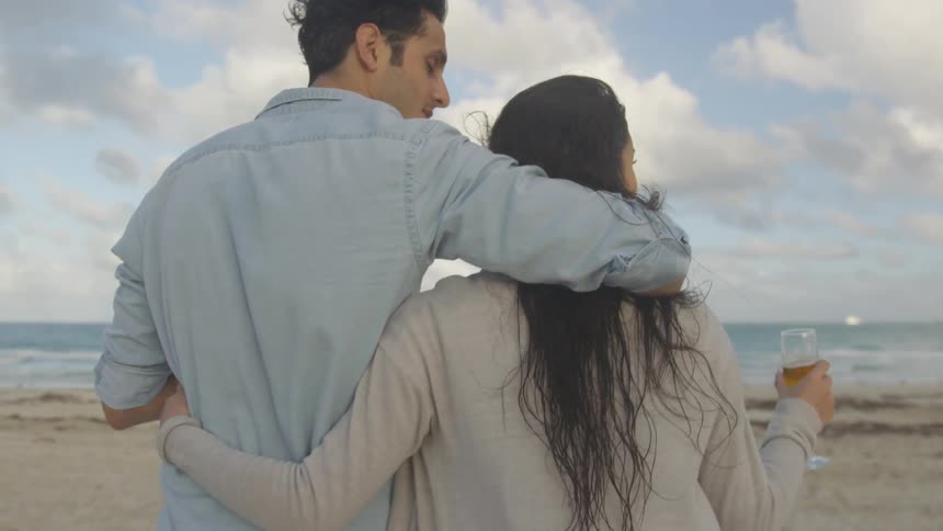 Man and woman walk on the beach with their arms around each other