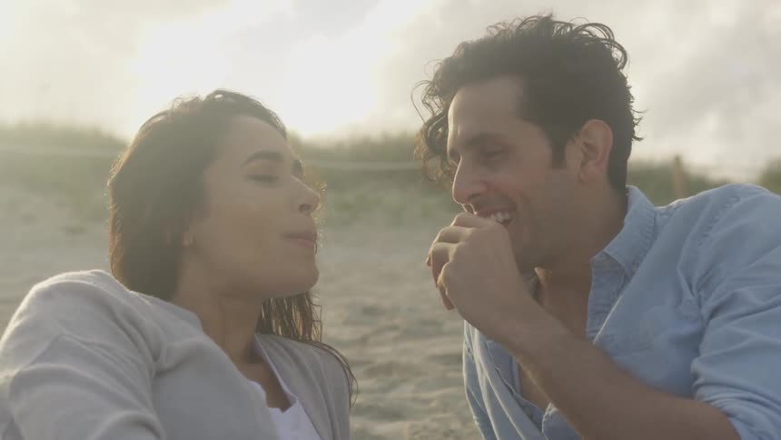 A man feeds a woman on the beach