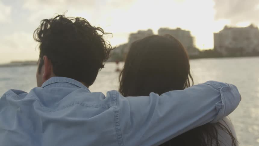 A man has his arm around a woman as they look out at the ocean