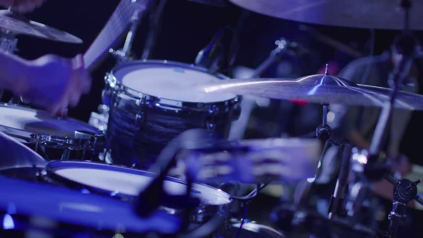 The man plays the drums on the dark stage