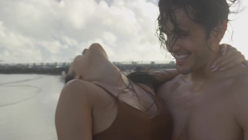 A man and a woman laugh and dance on the beach on a cloudy day