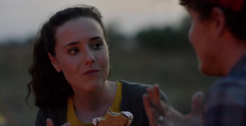 A man and woman eat s'mores at a campfire and talk