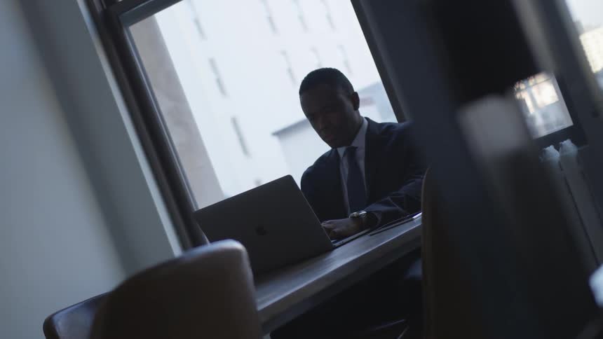Man sits at a table in an office typing on a laptop