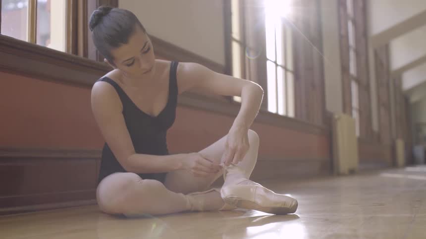 A ballerina ties her ballet shoe in a dance studio