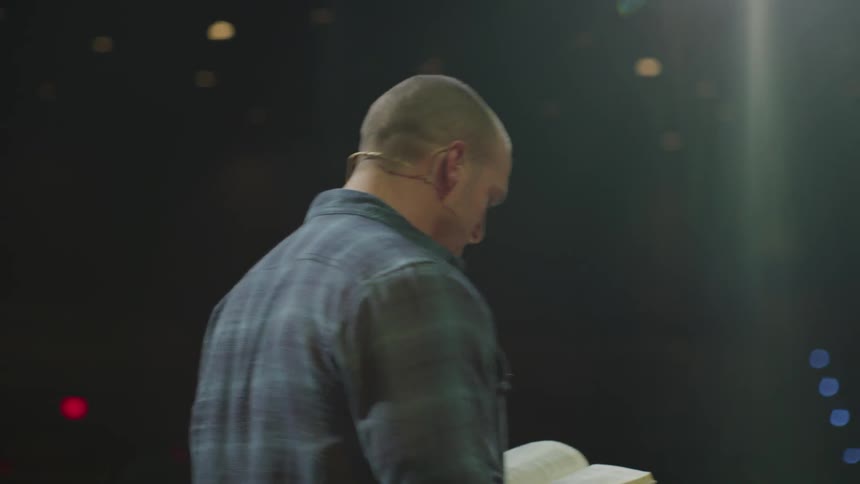 A man reads from a book on stage