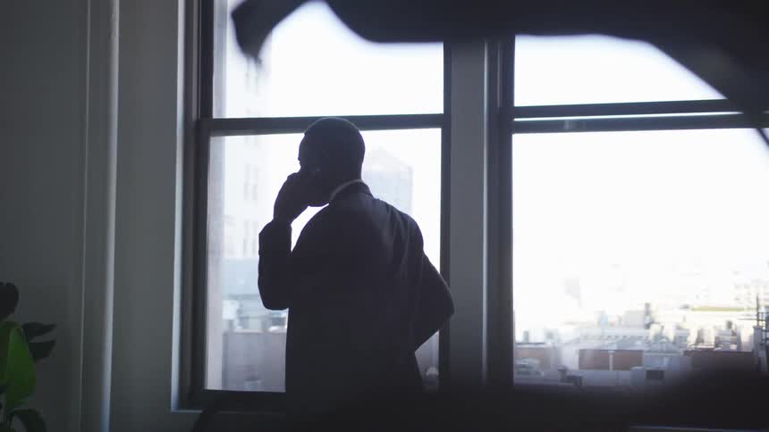A man in a suit talks on the phone while walking in an office