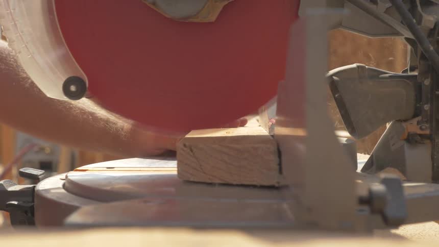 Construction worker is cutting piece of wood with miter saw