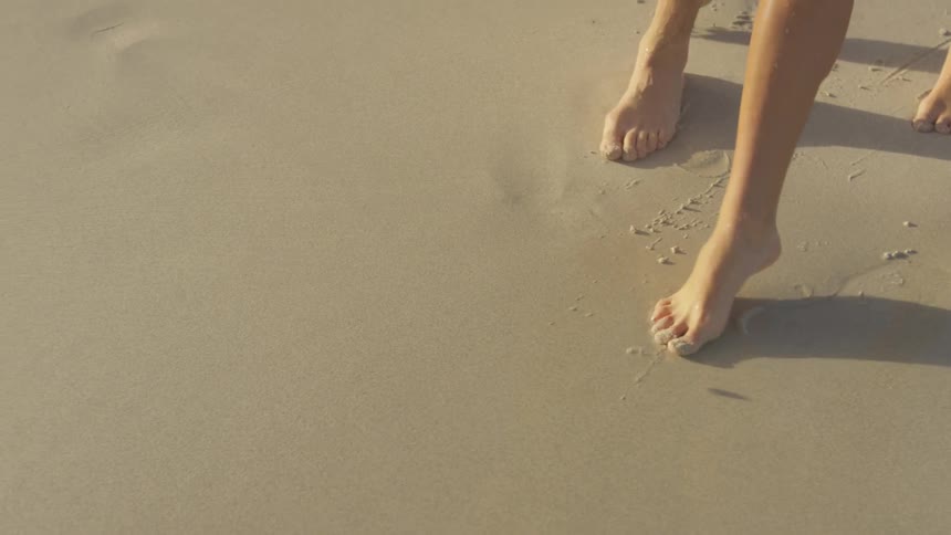 The bare feet of a man and woman walking in the sand