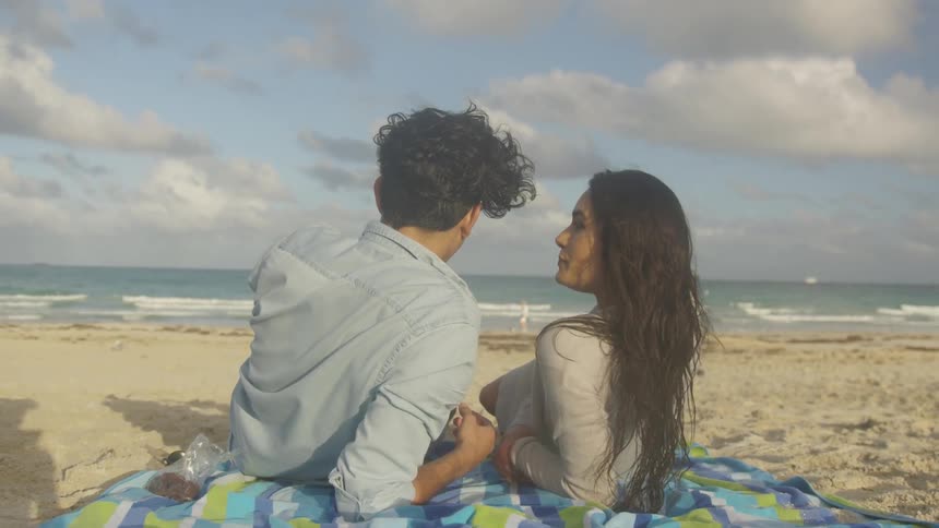A couple lean back on their beach towel and look at each other