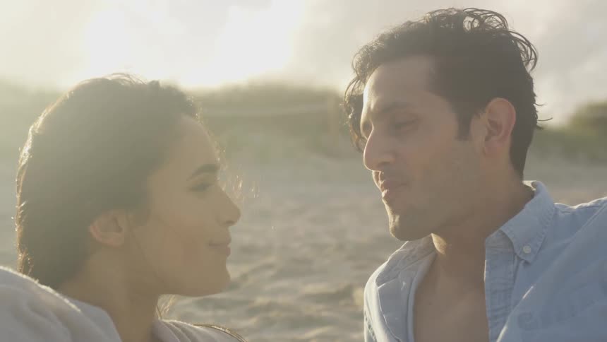 A man smiles as he places a piece of food in a woman's mouth on the beach on a cloudy day