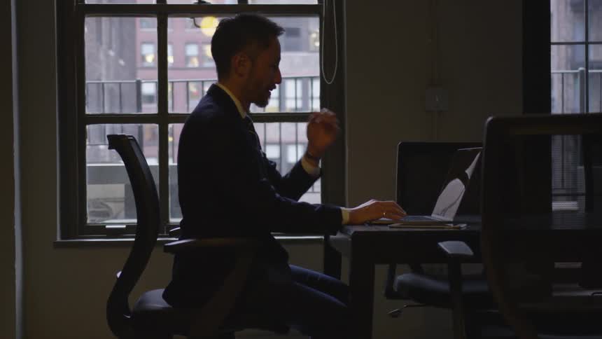 A businessman types on a laptop in an office