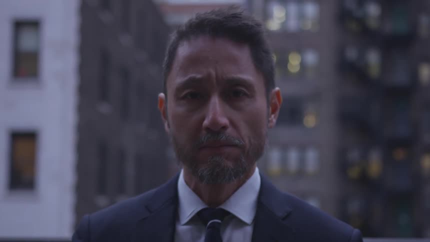 Man wearing a suit stands on a balcony in the city