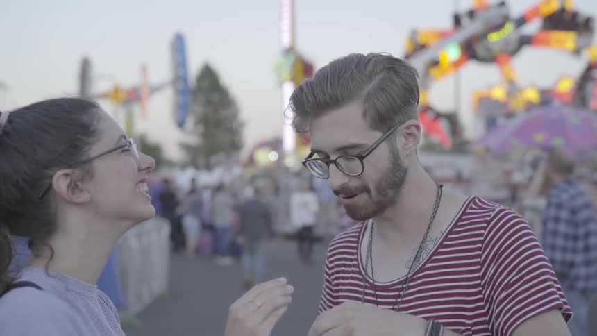 A couple feed food to each other at a carnival