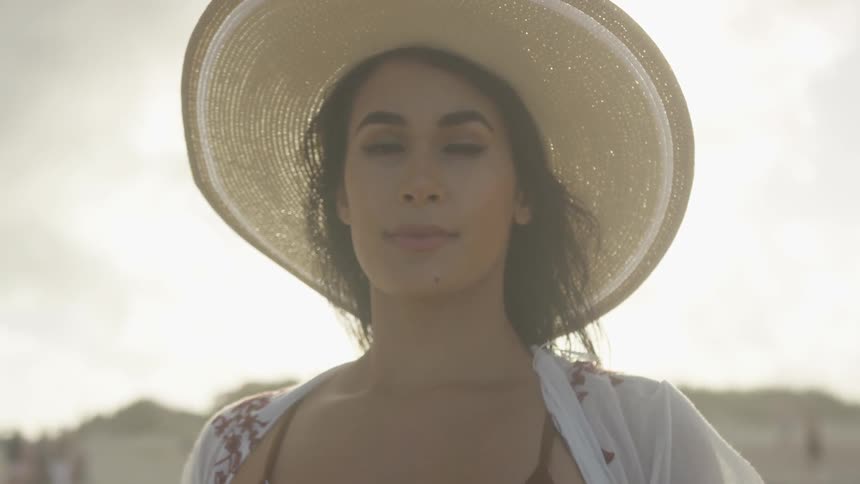 A woman adjusts her hat on the windy beach