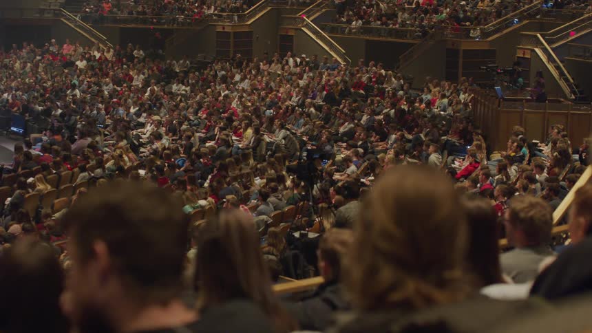 Large audience of people sit in an auditorium