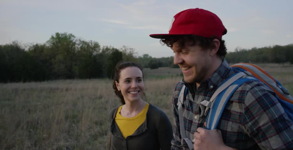 Smiling couple walking through a field carrying equipment