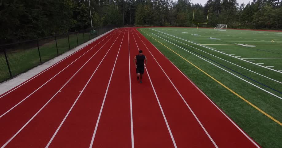 Man runs on a red track with a playing field next to it