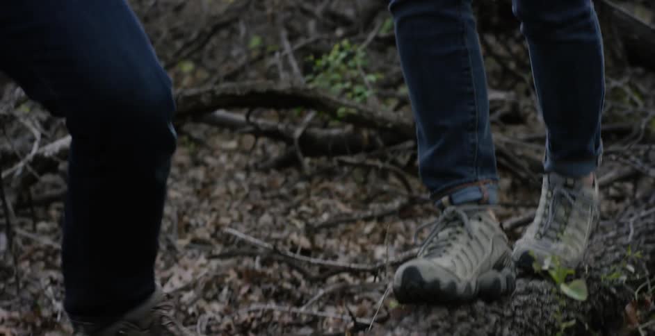 A man holds the hand of a woman walking on a log in a woody area