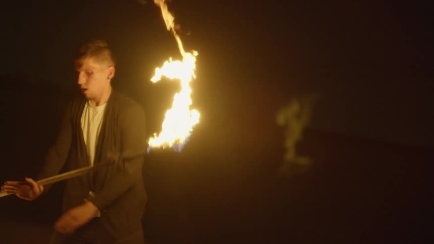 A man stands outside at night twirling a torch lit on both ends