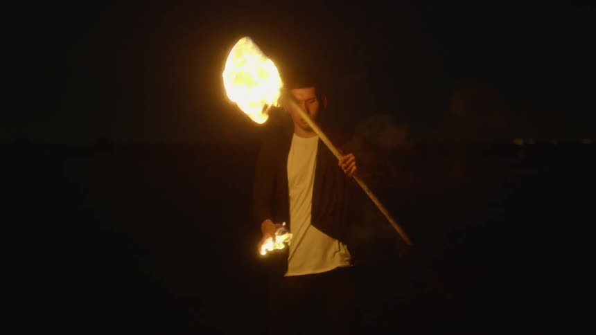 A man holds and lights a flaming torch outside at night