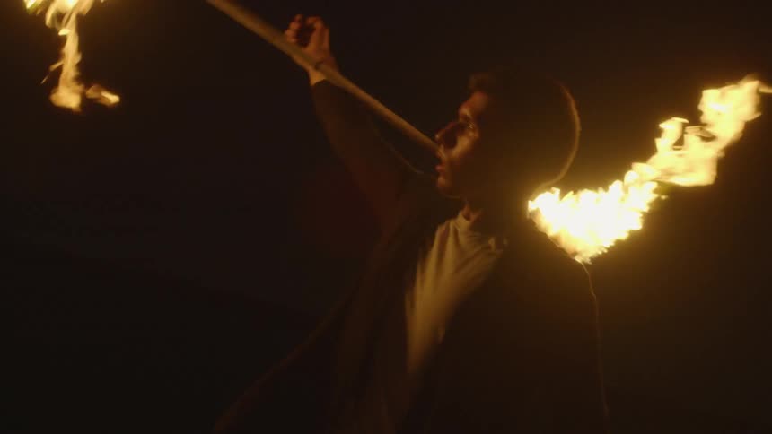 A man twirls a flaming baton at night