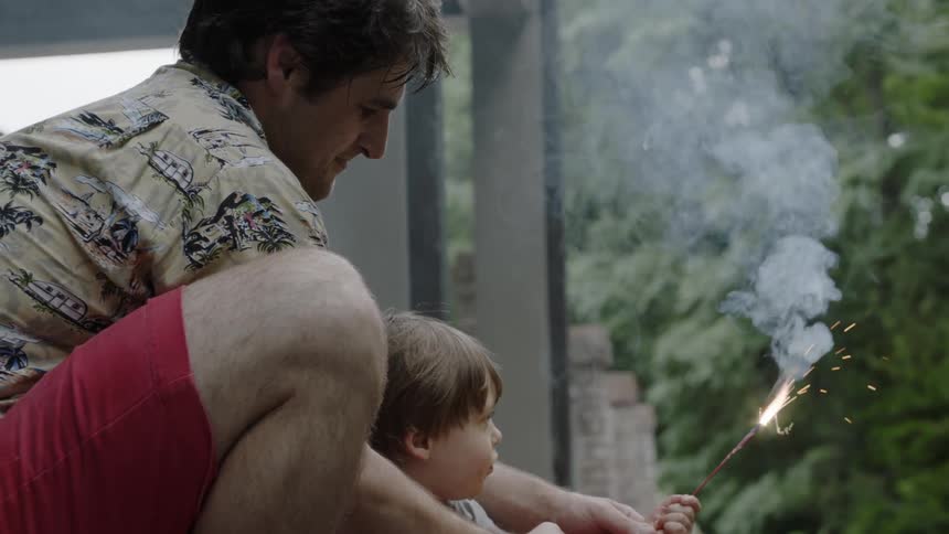 Man helps a child hold a small sparkler
