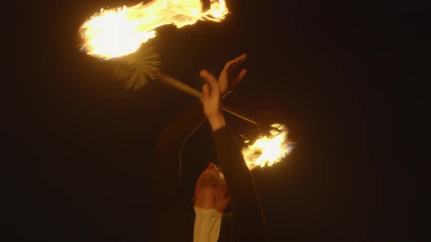 A man twirls a flaming baton at night