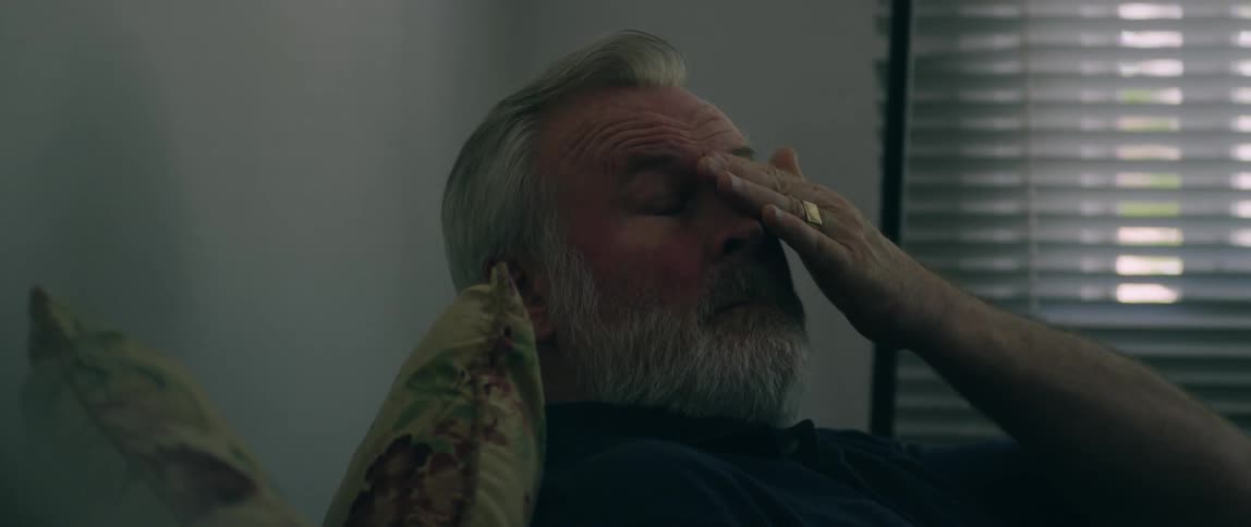 The man wipes his forehead on the couch