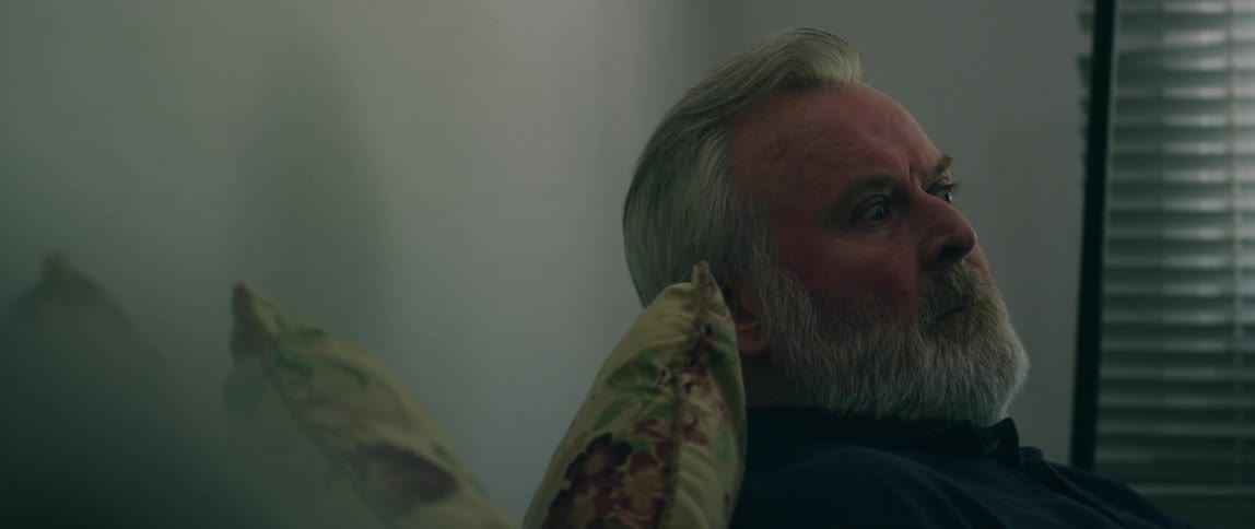 A man grimaces while leaning back against pillows