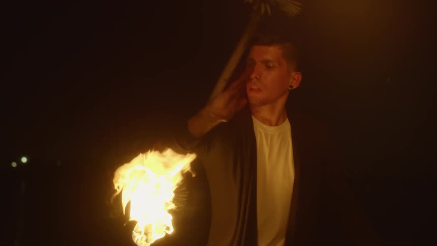 A man stands on the beach at night twirling a lit torch