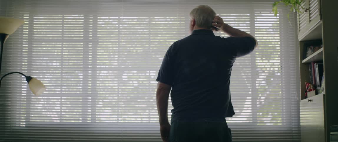 Man scratches his head as he looks towards the window blinds