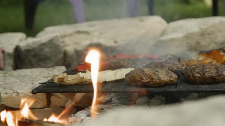 Burgers and veggies are cooked on a grill outside