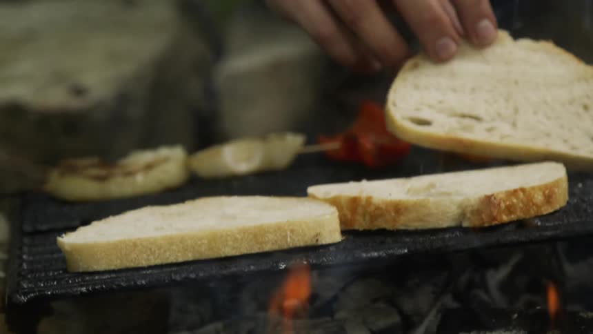 A man places bread slices on a flaming grill