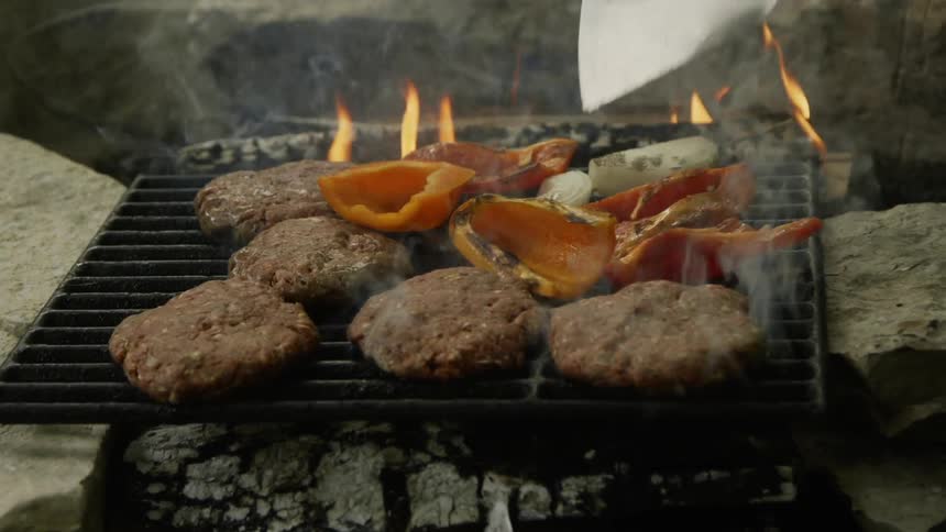 Peppers and burgers are cooking on a flaming grill